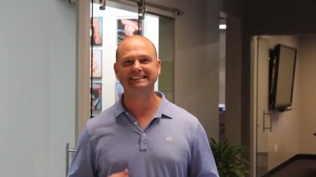 Man in a blue shirt standing in an office hallway describing about Advanced Leadership Program.